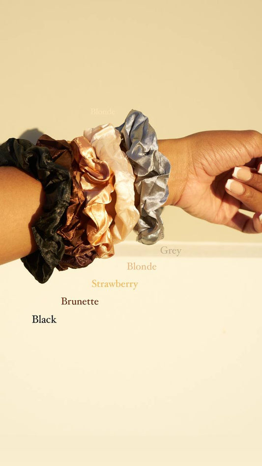 Satin scrunchies in black, brunette, strawberry, blonde, and grey on a wrist.